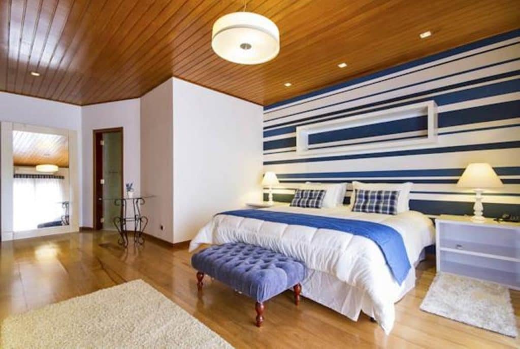 Quarto da pousada com cama de casal, parede colorida e mesas de cabeceira com abajur. 