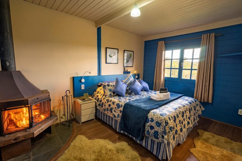 Quarto com lareira acesa e cama toda coberta com colcha azul 